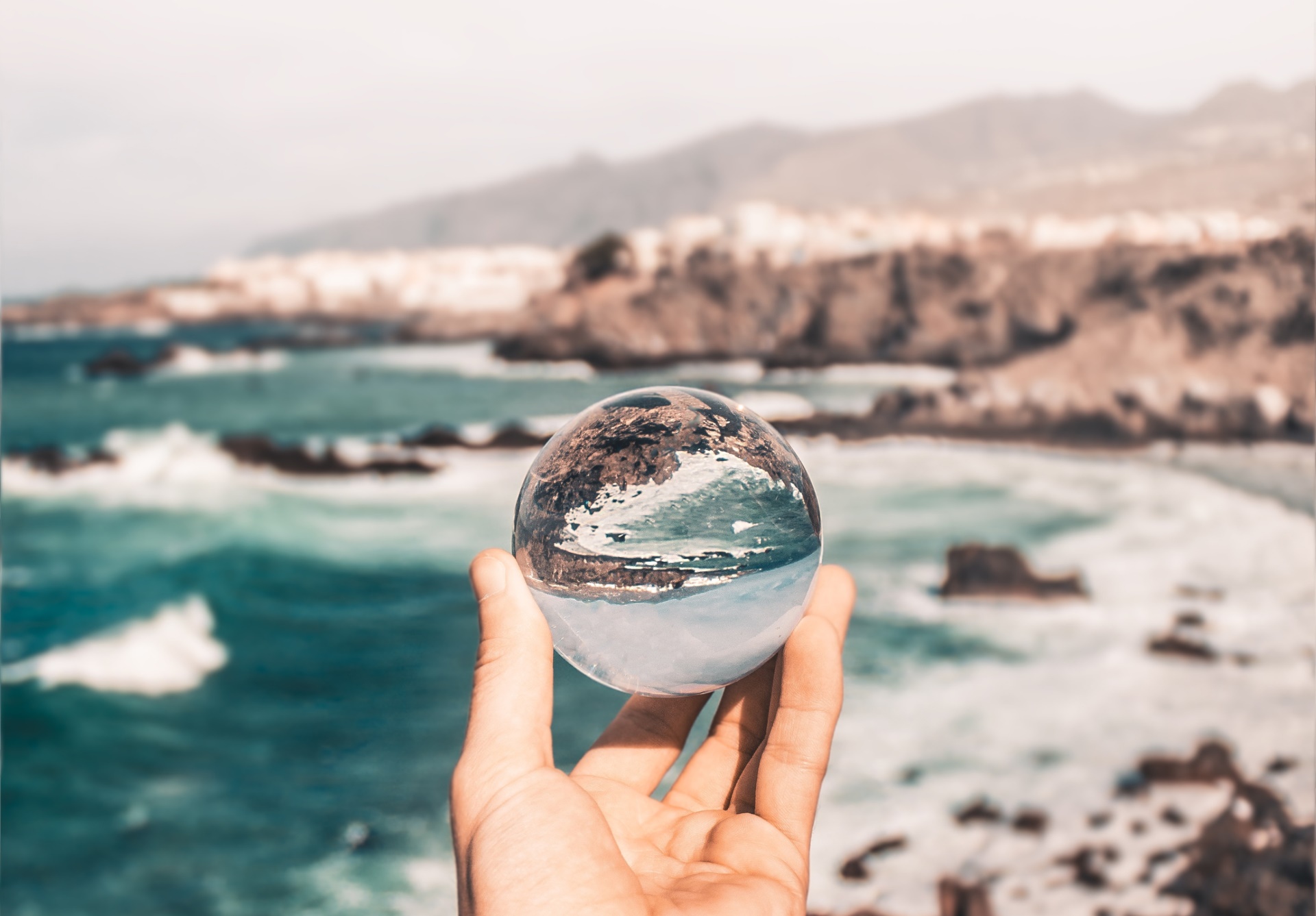 Hand lifting up a crystal ball near the ocean.