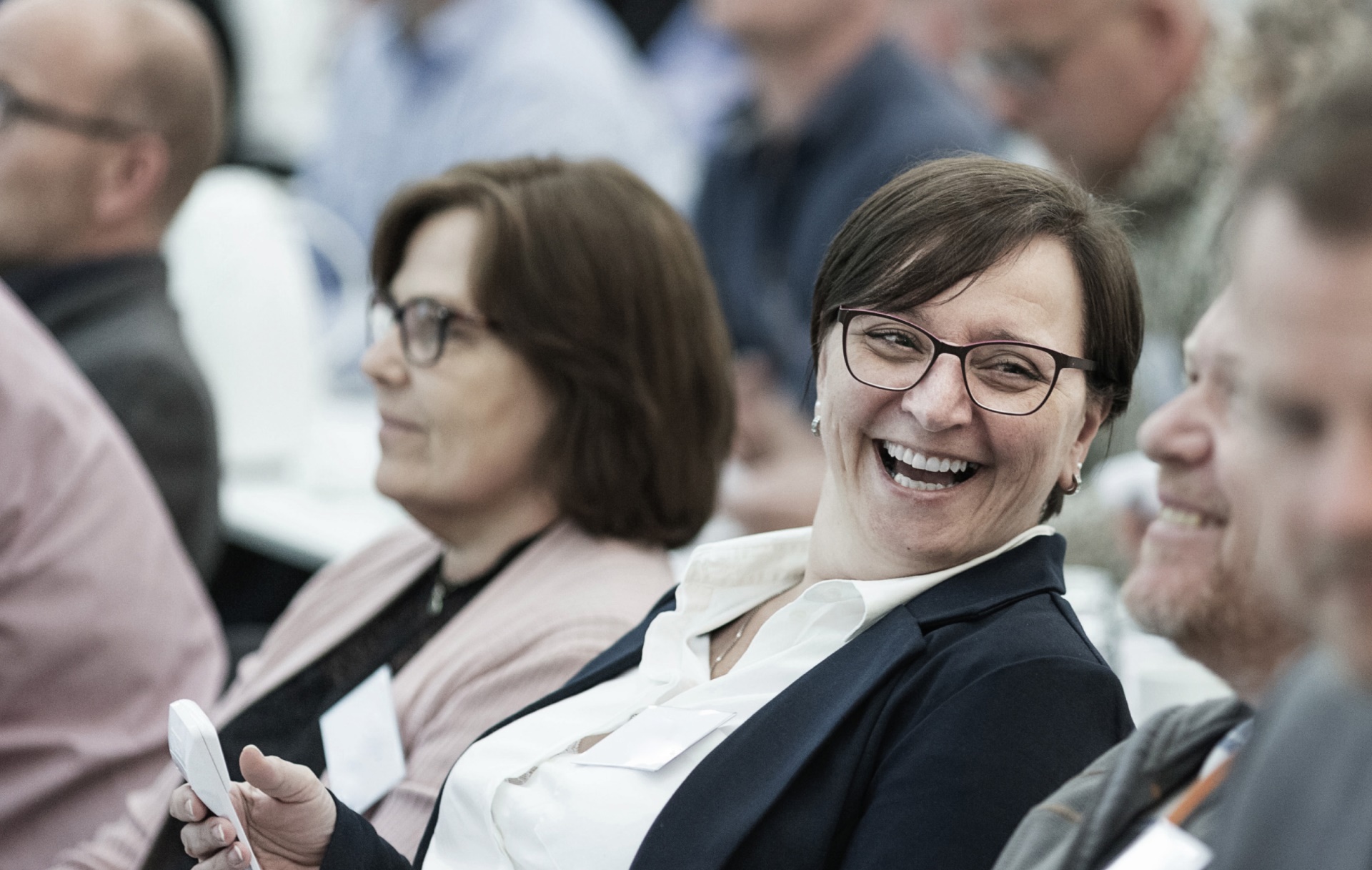 Business woman sitting in a crowd laughing.